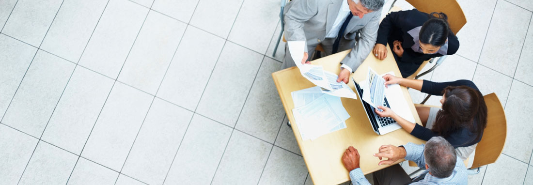 Overhead view of business people clustered around a small table reviewing paperwork