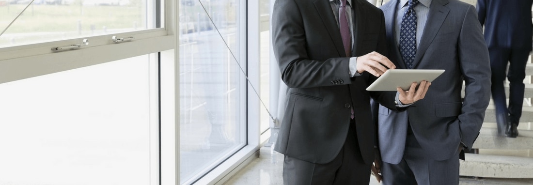 Two businessmen standing and looking at a tablet.